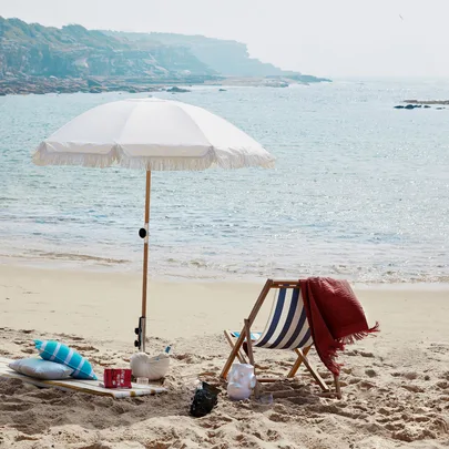 Beach scene with an umbrella, deck chair, and blanket by the sea. Perfect for a relaxing day by the ocean.