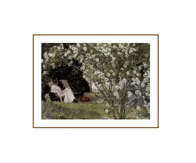 A person in a garden with white flowers, seated in a chair and reading.