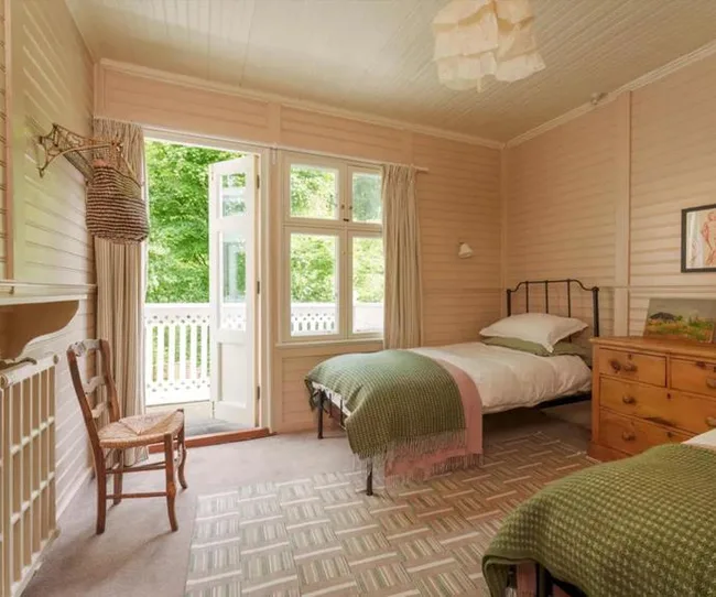 Cozy bedroom with two single beds, green blankets, a wooden chair, and an open door to a lush garden outside.