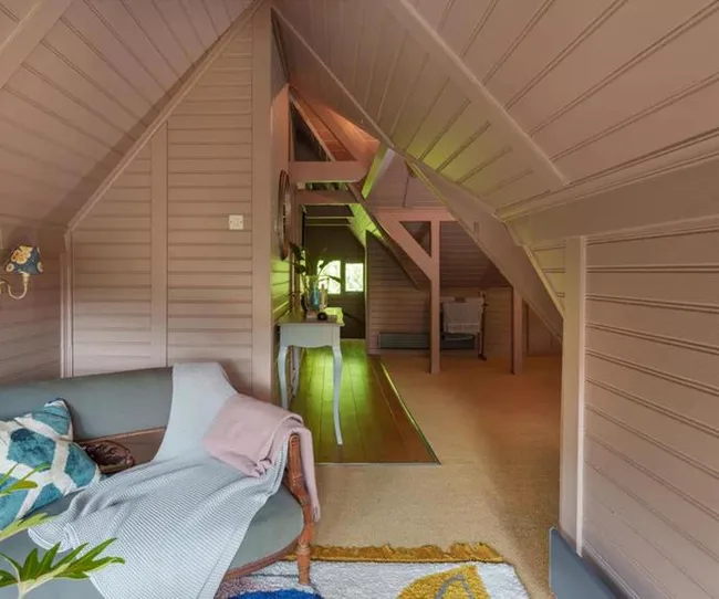 Cozy attic space with sloped wooden ceiling, a sofa with cushions and blanket, and a rug.
