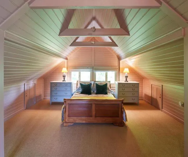 Cozily renovated attic bedroom with wooden bed, two dressers, and soft lighting.