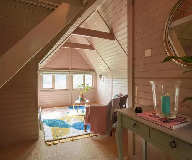 Cozy attic nook with a colorful rug, chair, small table, plants, and a mirror reflecting soft light.