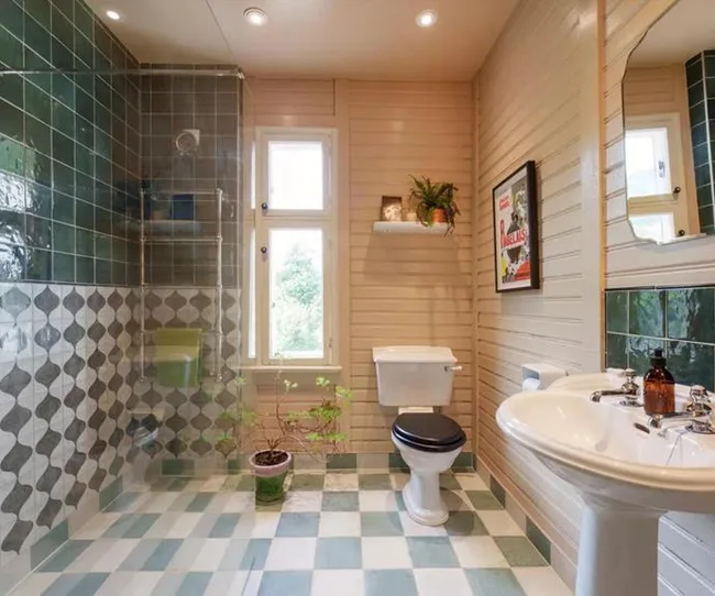 Bathroom with green tiles, shower, toilet, sink, potted plant, wall art, and checkered floor.