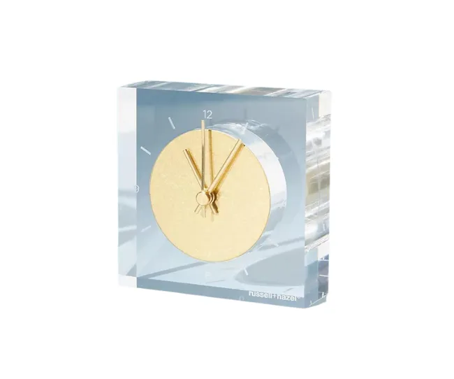 Gold clock encased in clear acrylic, angled view, with minimalist design and Russell+Hazel branding.