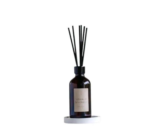 Dark glass bottle with black reed sticks, labeled "smoked lavender," on a white coaster.