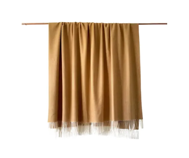 Tan cashmere scarf with fringe edges hanging on a rod.