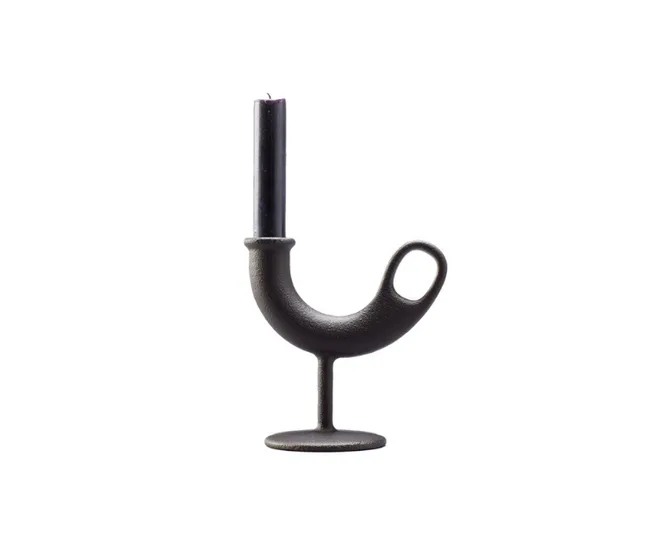 Curved black candlestick holder with a loop handle, holding a tall black candle on a white background.
