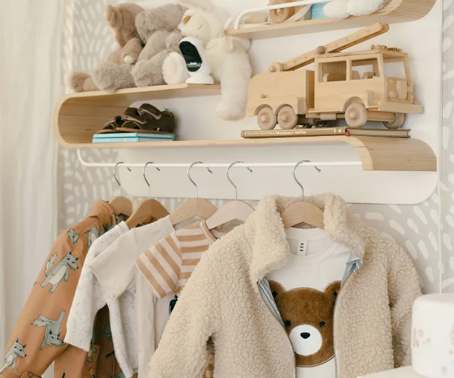Children's clothing and toys including teddy bear sweaters, wooden fire truck, and plush animals on shelves.