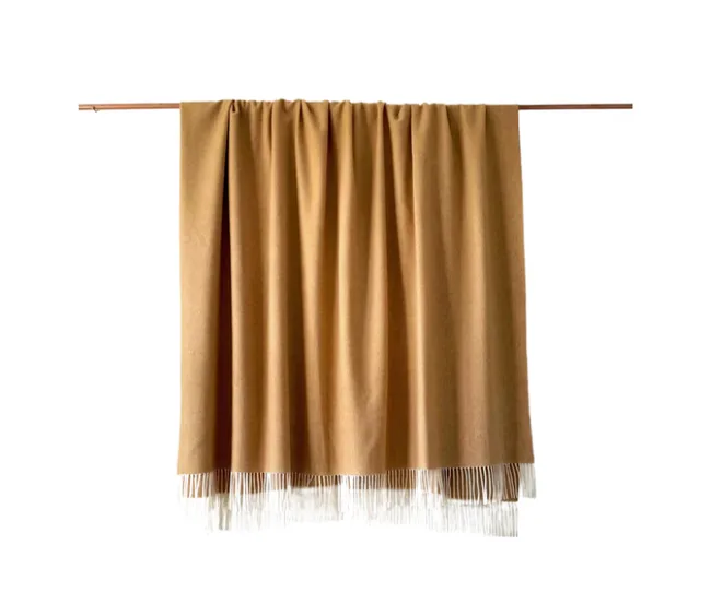 Brown blanket with fringe hangs over horizontal rod against white background.