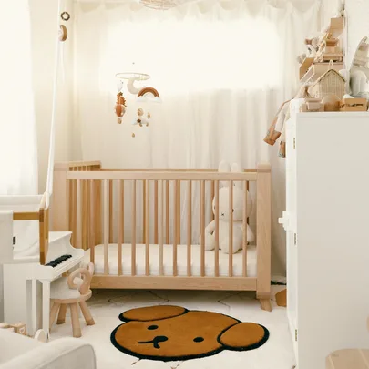 Cozy nursery with a wooden crib, a plush toy, and a mobile. A rug with a cute bear face pattern on the floor.