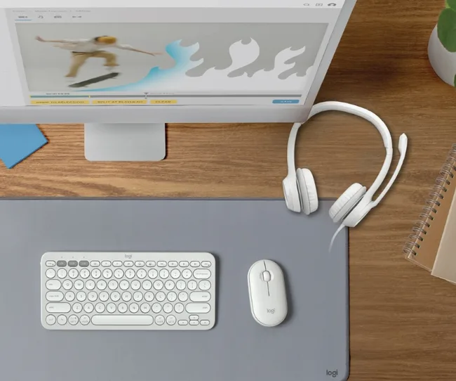 A workspace with Logitech keyboard, mouse, and headset on a wooden desk, and a monitor showing a skateboarding video.