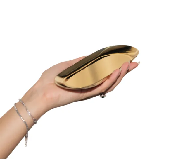 A hand holding a glossy, gold metallic dish with a curved design.