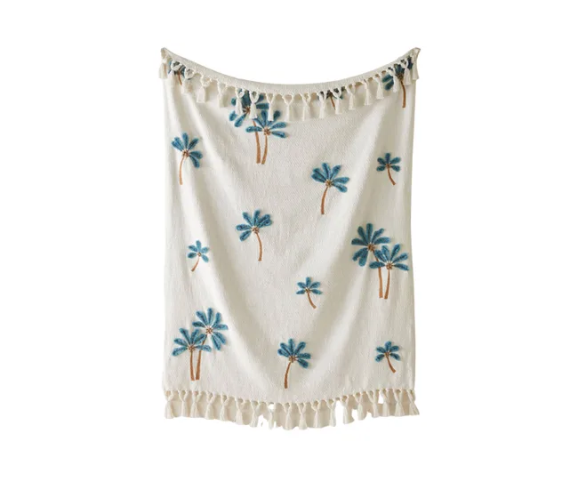 A white towel with blue palm tree prints and tasseled edges.