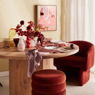 Round wooden table set with red decor, flowers, and velvet chairs in a warmly lit dining room.