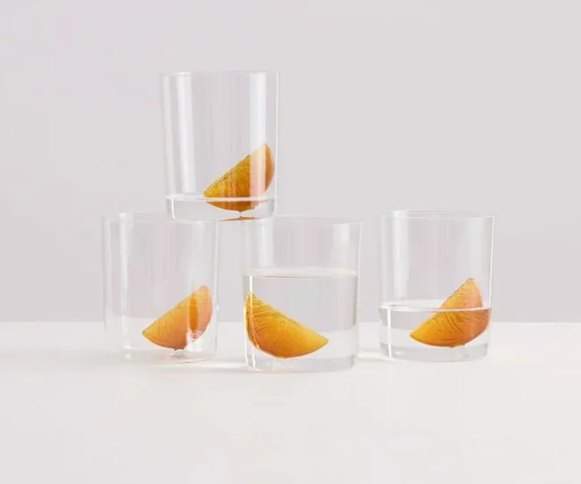 Four glasses of water with orange slices, arranged on a white surface.