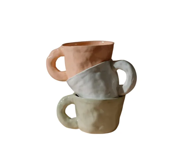 Three stacked ceramic mugs in pastel colors: pink, white, and green, with a textured surface.