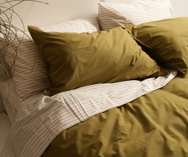 Olive green duvet with white striped sheets and pillows in a neatly made bed.