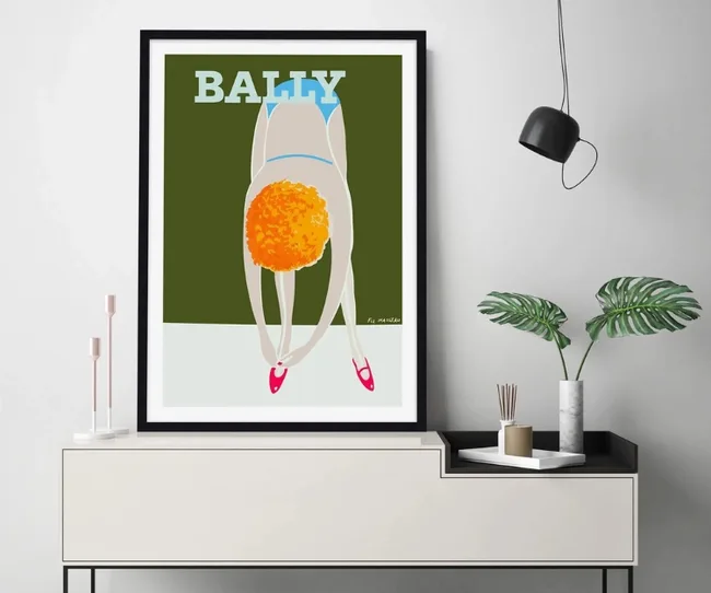 Framed artwork of a dog in pink shoes, labeled "Bally," on a console with plants and a lamp.