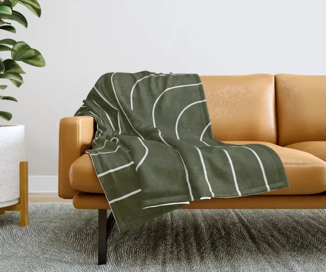Olive green blanket with white lines on a tan sofa, next to a plant.