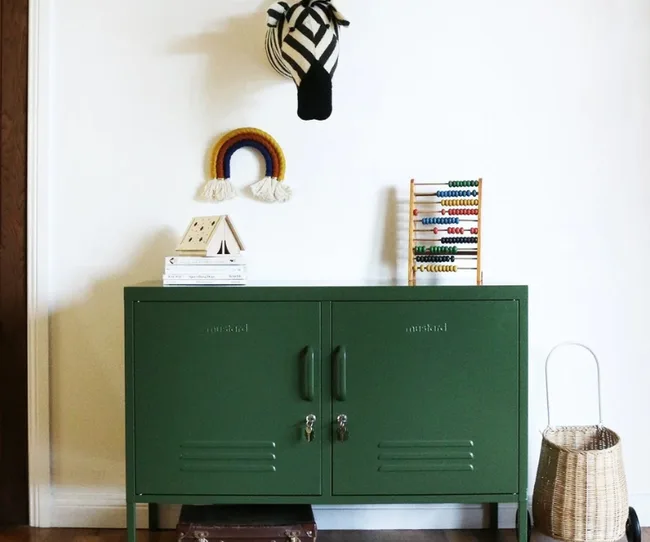 Green cabinet with abacus on top, wall-mounted zebra head, and woven rainbow. Basket and books are nearby.
