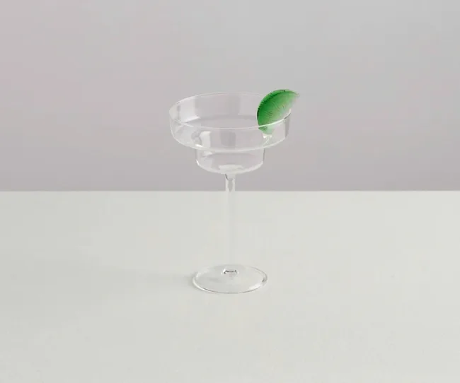 Clear margarita glass with a green lime wedge garnish on a white surface.