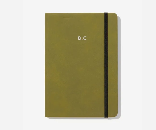 Olive notebook with "B.C" embossed, secured by a black elastic band.