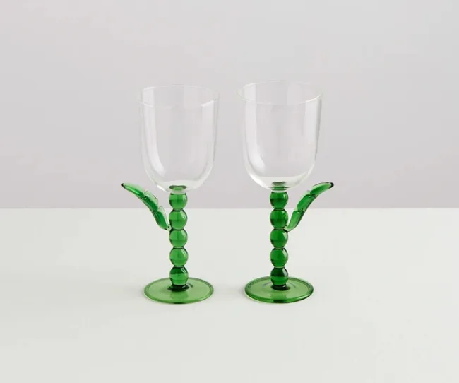 Two clear wine glasses with decorative green stems and bases on a white surface.