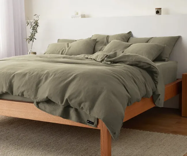 Olive green bedding set on a wooden bed frame in a cozy, well-lit bedroom.