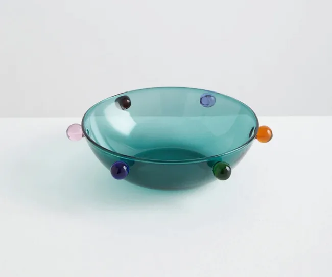 Teal glass bowl with multicolored bead accents on a white surface.
