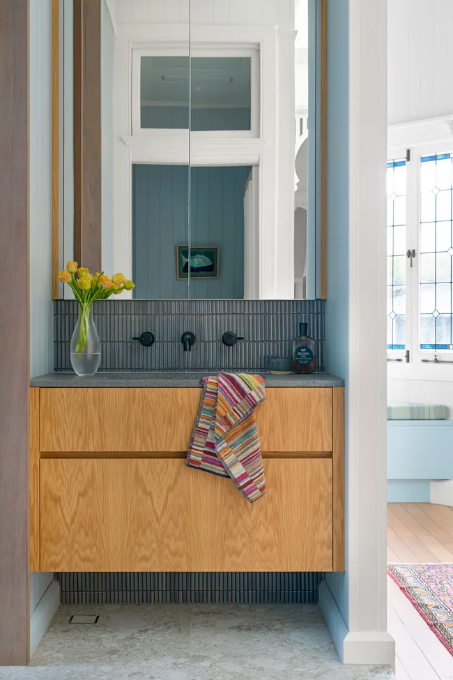 Modern bathroom vanity with wooden drawers, striped towel, vase of yellow flowers, and black fixtures.