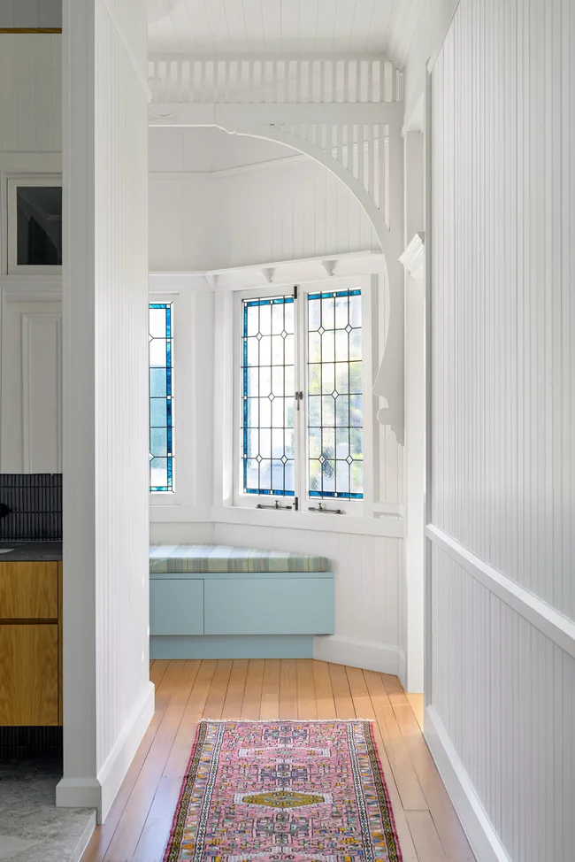 Bright hallway with wood floor, stained glass windows, a pastel blue bench, and a pink patterned rug.