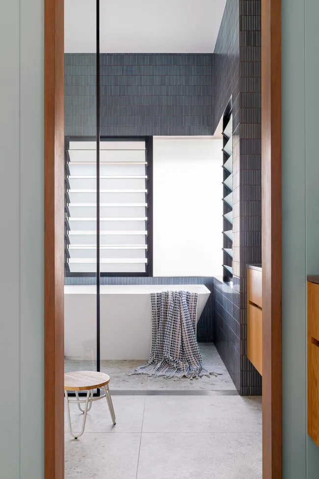 Modern bathroom with a white bathtub, dark tiled walls, and a checkered towel draped over the tub edge.