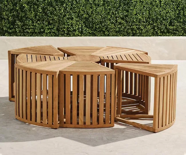 Wooden circular seating set with separate segments on a paved surface, greenery in the background.