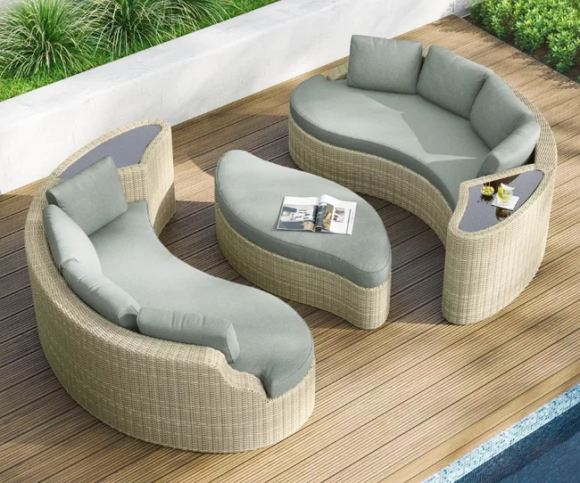 Outdoor wicker patio set with curved sofas and glass-topped table on wooden deck, next to a pool and garden.