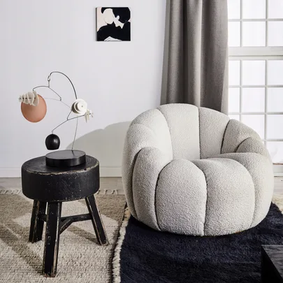 Cozy white armchair on a black rug beside a small black table with a decorative piece, in a well-lit room.