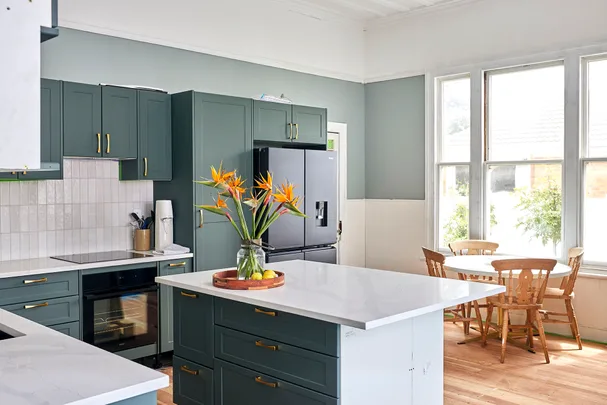 Stylish kitchen with green cabinets, black fridge, white countertops, and a vase with flowers on the island.