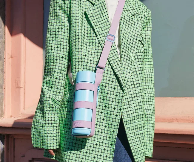 A woman in a green jacket wearing a lilac Cactus Leather Bottle Holder, holding a blue bottle