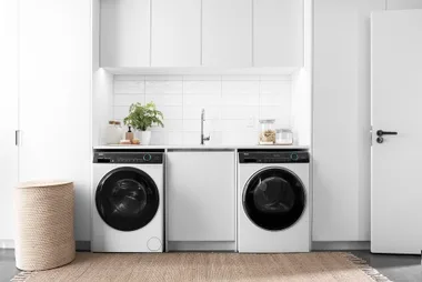 Laundry room with front-loading washer, dryer, and countertop with plants and jars.