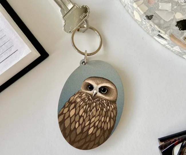 Keychain with an illustrated owl on a table, next to a notebook and other objects.