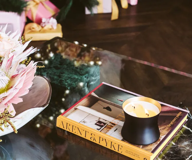 A black candle on a book titled "Arent & Pyke" on a table near flowers and gift boxes.
