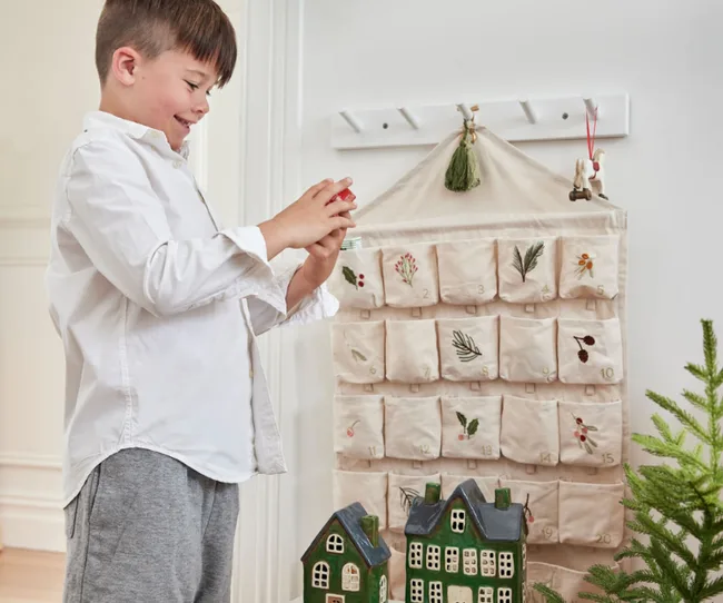 Boy in white shirt looks at toy near fabric advent calendar and ceramic houses.