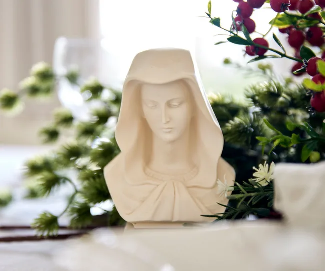 Bust of a woman in a hooded cloak surrounded by greenery and red berries.