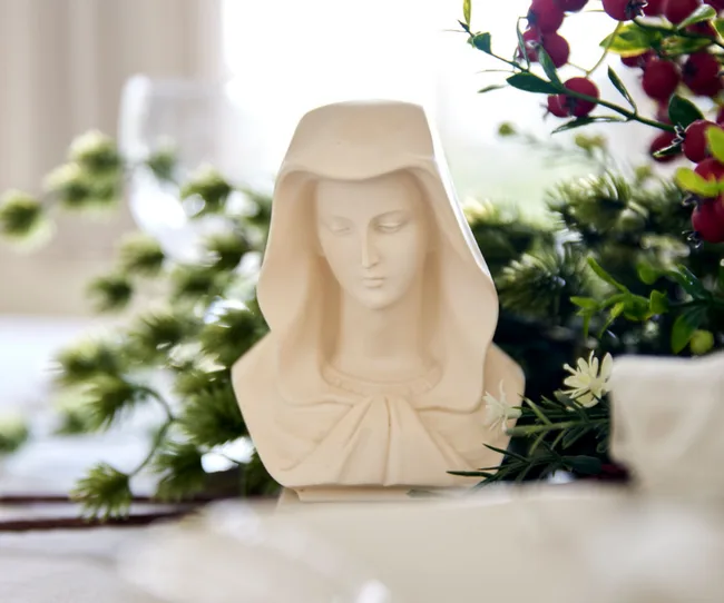 Bust of a veiled woman in a serene expression, surrounded by green foliage and red berries.