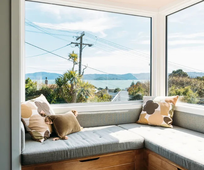 Cozy window seat with cushions, overlooking a scenic view with trees, power lines, and mountains in the distance.