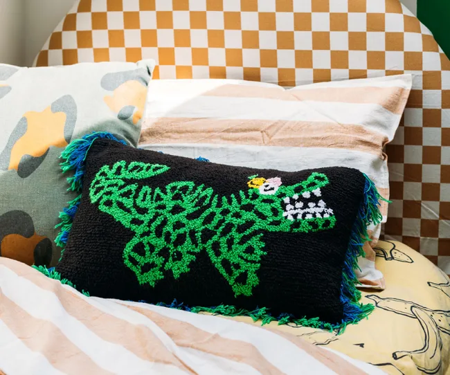 Colorful bedding with a checkered headboard and pillows, including one with a green crocodile design.