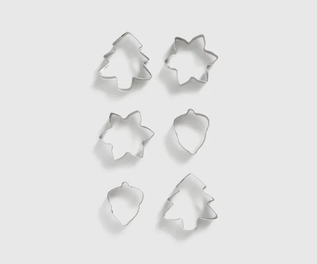 Six metal cookie cutters in shapes of trees, leaves, and acorns on a light background.