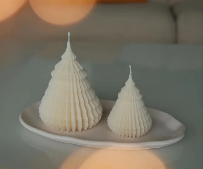 Two cream-colored, pyramid-shaped candles on a white plate, with warm ambient lighting in the background.