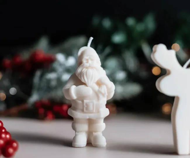 Santa-shaped candle with festive background, featuring greenery and red berries.