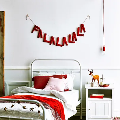 Bedroom with festive "Fa La La La La" banner, red accents, and reindeer figurine on white nightstand.