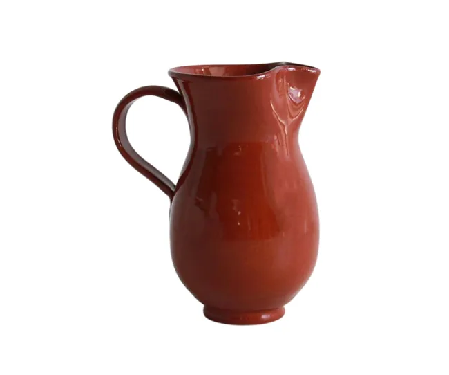 Red ceramic pitcher with a curved handle on a white background.